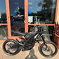 Black Dirt Bike with Carbon Fiber Fenders Surron in front of store Hyper Rides