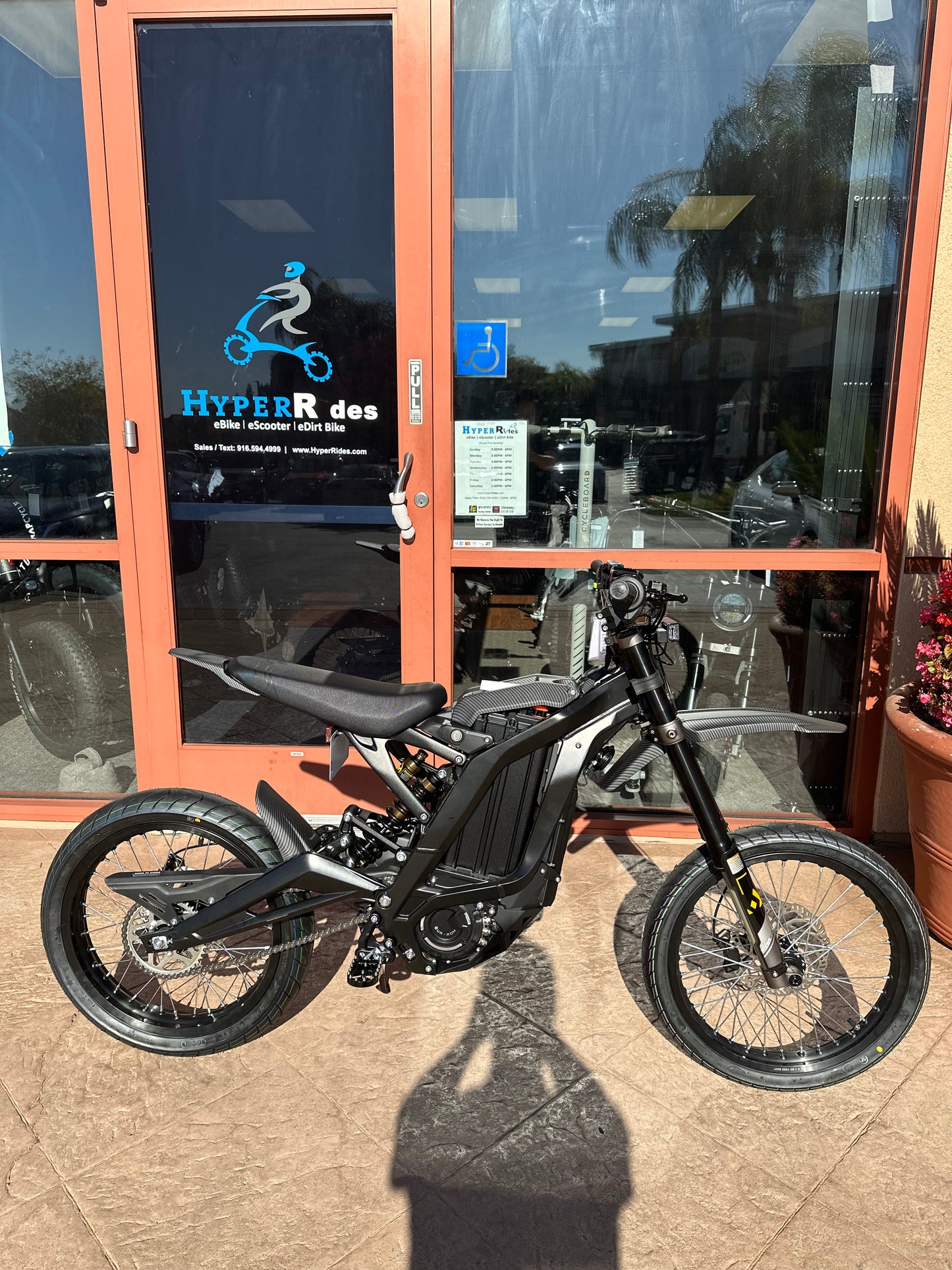 Black Dirt Bike with Carbon Fiber Fenders Surron in front of store Hyper Rides